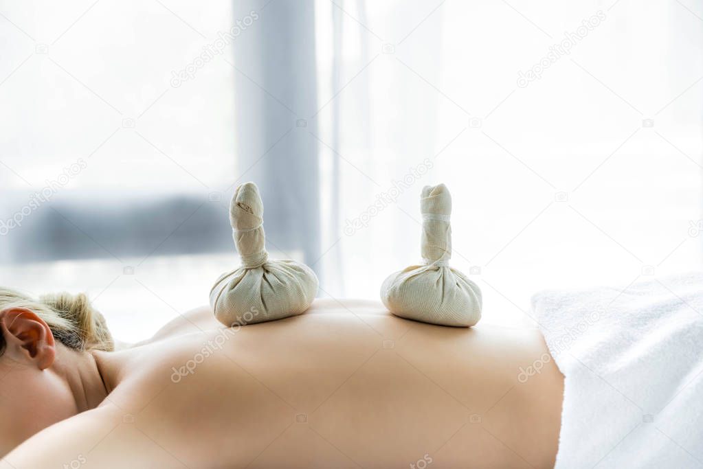 woman lying on massage mat with herbal balls on back 