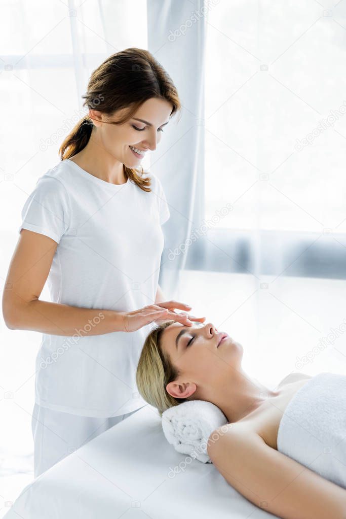smiling masseur doing face massage to attractive woman in spa 
