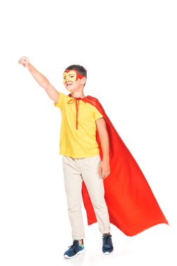 full length view of kid in mask and hero cloak holding fist up isolated on white clipart