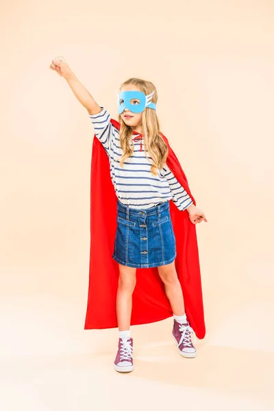 full length view of child in mask and hero cloak holding fist up on pink