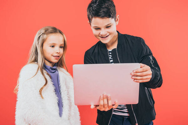 two smiling kids using laptop isolated on red