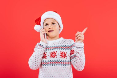 kırmızı izole akıllı telefon konuşurken santa şapka hoşnutsuz çocuk