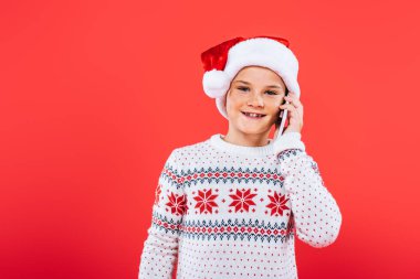 kırmızı izole akıllı telefon konuşurken santa şapka gülümseyen çocuk ön görünümü