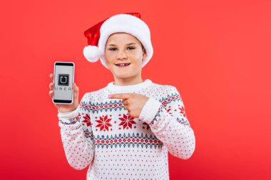 Kiev, Ukrayna - 9 Eylül 2019: ekranda uber uygulaması ile akıllı telefon parmak ile işaret santa şapka gülümseyen çocuğun ön görünümü