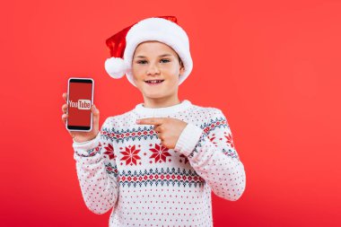 Kiev, Ukrayna - 9 Eylül 2019: ekranda youtube uygulaması ile akıllı telefon parmak ile işaret santa şapka gülümseyen çocuk ön görünümü