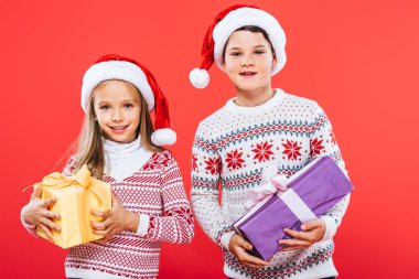 kırmızı izole hediyeler ile santa şapkalı iki gülümseyen çocukların ön görünümü
