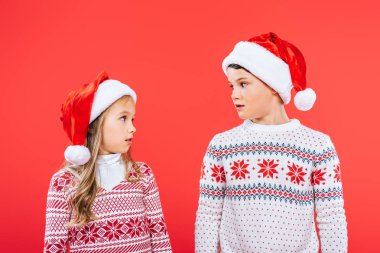 noel baba şapkalı iki sürpriz çocuk birbirlerine kırmızı izole bakarak