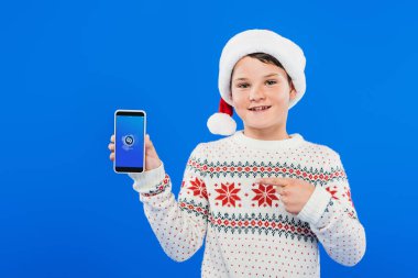 Kiev, Ukrayna - 9 Eylül 2019: mavi ekranda shazam uygulaması ile akıllı telefon parmak ile işaret santa şapka gülümseyen çocuğun ön görünümü