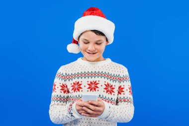 mavi izole akıllı telefon kullanarak santa şapkalı çocuğun ön görünümü