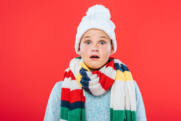 front view of shocked kid in hat and scarf isolated on red
