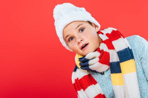 shocked child in hat and scarf isolated on red