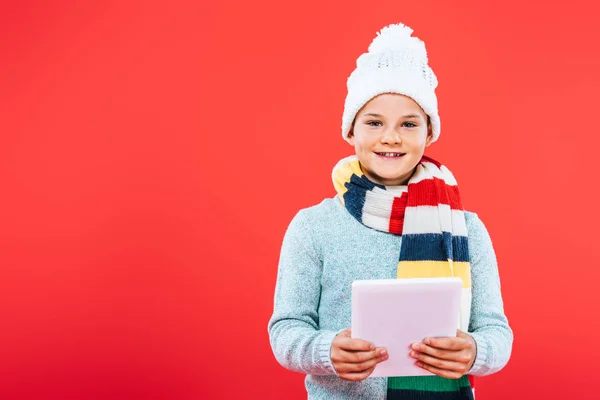 微笑的孩子在帽子和围巾前视图使用数字平板电脑隔离在红色 — 图库照片