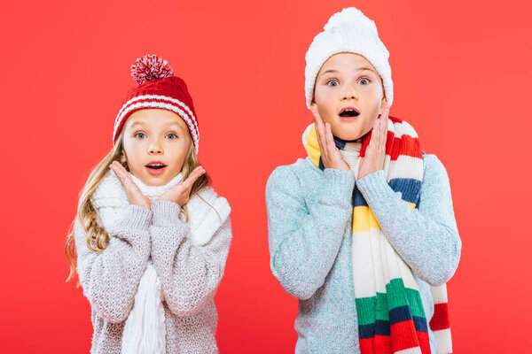 front view of two shocked kids in winter outfits isolated on red