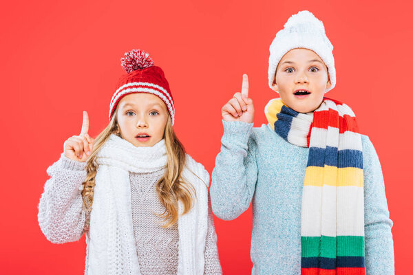 front view of two shocked kids in winter outfits showing idea signs isolated on red