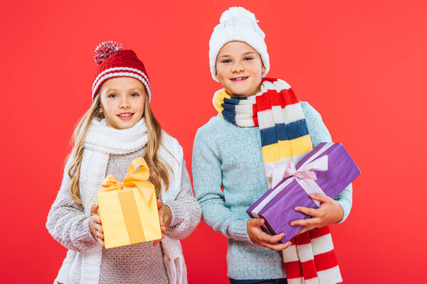 front view of two kids in winter outfits holding presents isolated on red