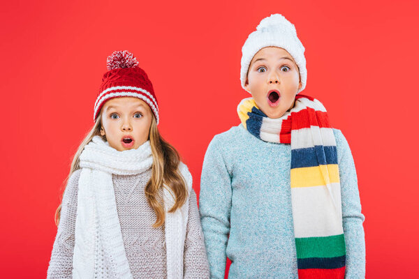 front view of two shocked kids in winter outfits isolated on red
