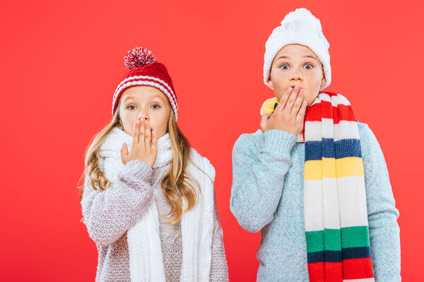 front view of two shocked kids in winter outfits isolated on red