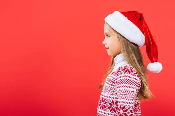 Widok Boku Uśmiechnięty Dzieciak Swetrze Kapelusz Santa Wyizolowany Czerwono — Zdjęcie stockowe
