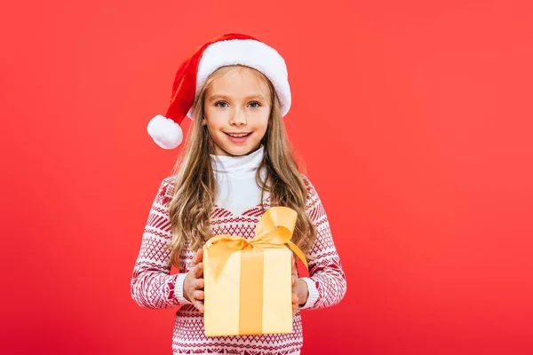 赤で孤立したプレゼントを持つサンタ帽子の笑顔の子供の正面図 — ストック写真