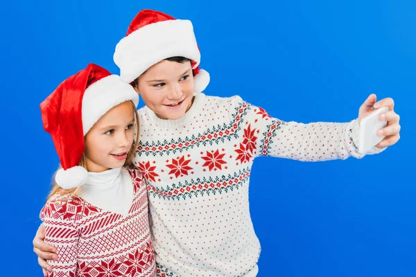 Two Smiling Kids Santa Hats Taking Selfie Isolated Blue — Stock Photo, Image
