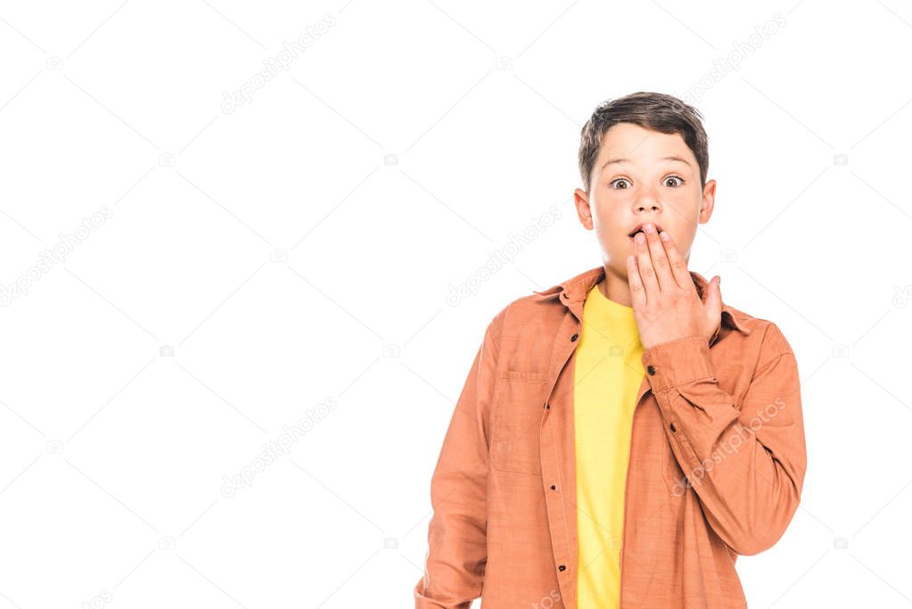 front view of shocked kid in casual outfit covering mouth with hand isolated on white