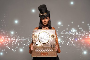 Silindir şapkalı steampunk kadın. Gözlüklü. Gri renkli, ışıldayan dijital illüstrasyonlu klasik dizüstü bilgisayar gösteriyor.