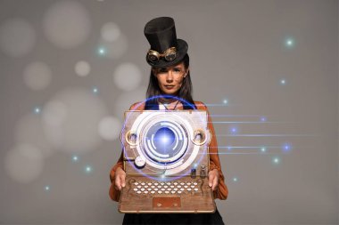 Silindir şapkalı steampunk kadın. Gözlüklü. Gri renkli, ışıldayan dijital illüstrasyonlu klasik dizüstü bilgisayar gösteriyor.