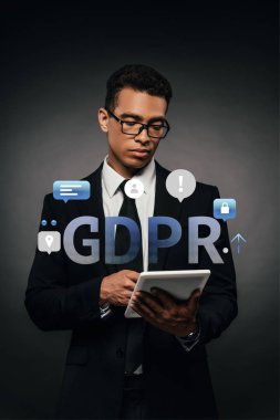 african american businessman in glasses using digital tablet on dark background with gdpr illustration clipart