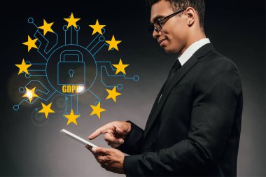 Gülümseyen Afro-Amerikan iş adamının karanlık arka planda dijital tablet kullanarak GDPR illüstrasyonu kullanmasının yan görüntüsü