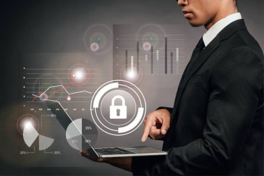 Afrika kökenli Amerikalı iş adamının karanlık arka planda internet güvenliği illüstrasyonuyla dizüstü bilgisayar kullandığına dair kısmi görüş