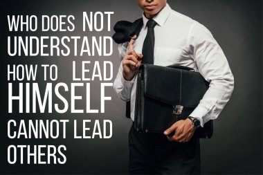 cropped view of african american businessman with leather briefcase and who does not understand how to lead himself cannot lead others lettering clipart