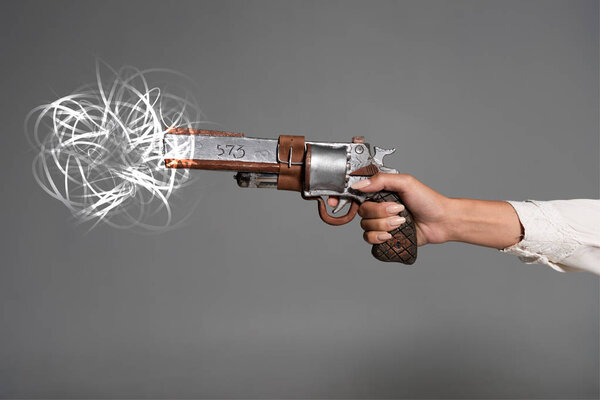 cropped view of woman shooting from vintage revolver isolated on grey