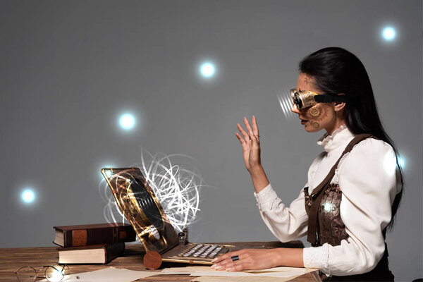 стимпанк женщина в очках размахивая рукой во время видео-чата с светящимися цифровыми иллюстрациями изолированы на сером
