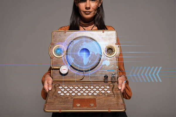 cropped view of steampunk woman in top hat with goggles showing vintage laptop with digital map isolated on grey