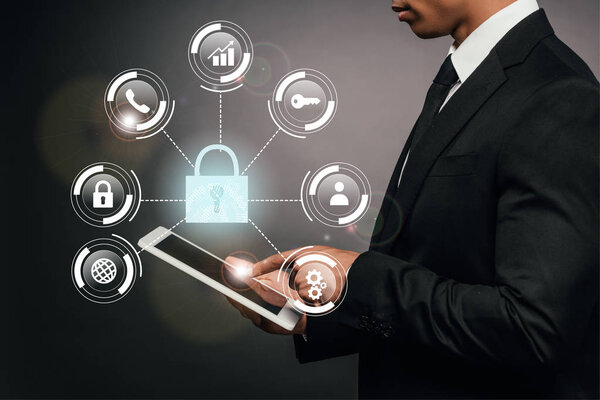 partial view of african american businessman using digital tablet on dark background with internet security illustration