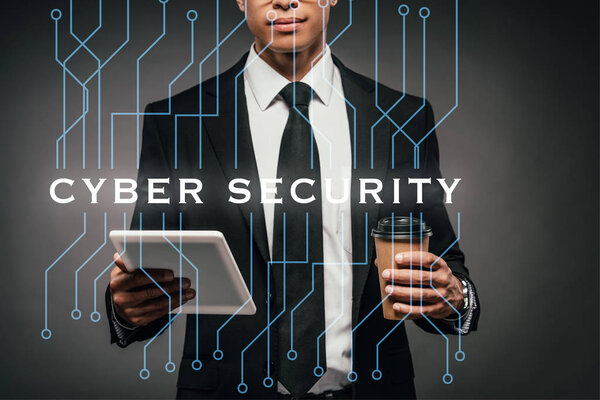 частичный взгляд на африканского американского бизнесмена, держащего кофе, чтобы пойти и цифровой планшет на темном фоне с иллюстрацией кибербезопасности
