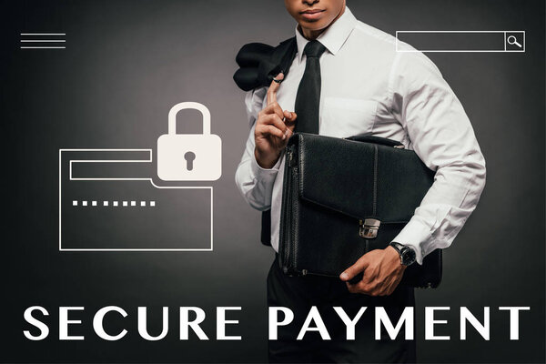cropped view of african american businessman holding blazer and leather briefcase on dark background with secure payment illustration