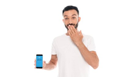 Kyiv, Ukrayna - 3 Eylül 2019: beyaz ekranda izole edilmiş Skype uygulaması ile ağzını kapatan ve akıllı telefonu elinde tutan şaşırmış adam 