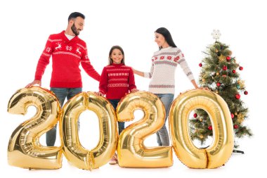 Balonların yanında duran süveterli mutlu bir aile ve beyaz üzerinde izole edilmiş noel ağacı. 