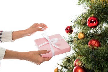 Kırpılmış, elinde pembe bir hediye olan bir kadının Noel ağacının yakınındaki beyaz bir odada izole edilmiş görüntüsü. 
