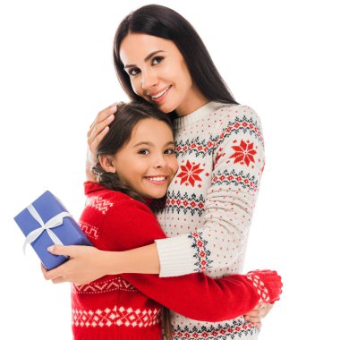 happy mother hugging daughter and holding preset isolated on white  clipart