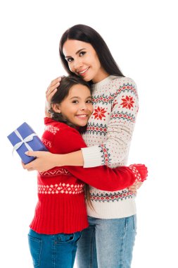 cheerful mother hugging daughter and holding preset isolated on white  clipart
