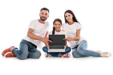 Beyaz tişörtlü neşeli ebeveynler, beyaz tişörtlü, kızına yakın, boş ekranlı, dizüstü bilgisayarı işaret ediyorlar. 