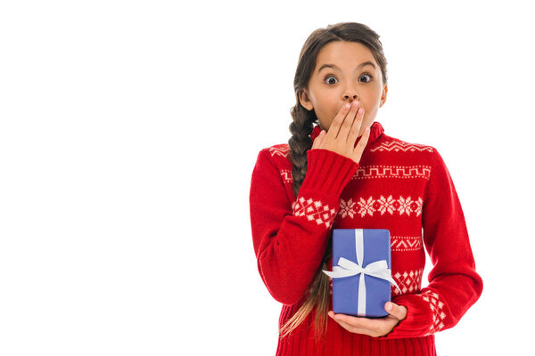 удивленный ребенок в свитере держит настоящее и покрывает рот изолирован на белом
 