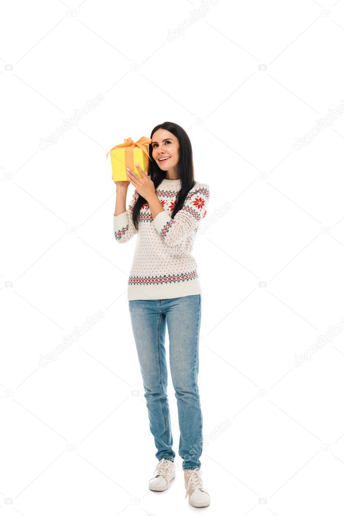 smiling woman in sweater holding gift box while standing  isolated on white 