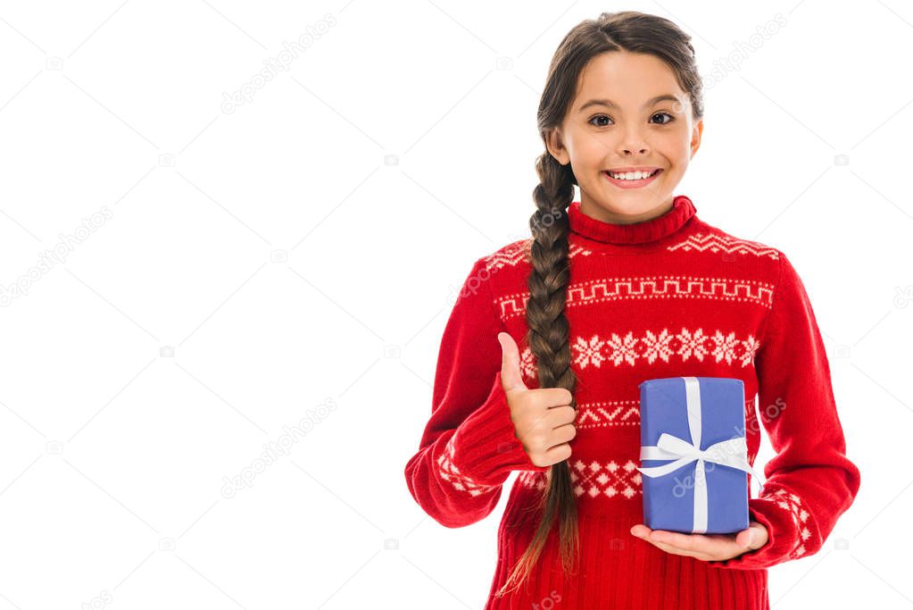 happy kid in sweater holding present and showing thumb up isolated on white 
