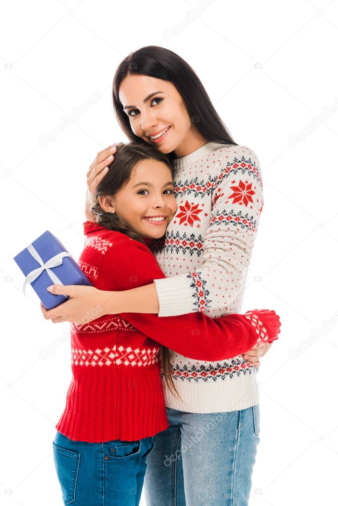 cheerful mother hugging daughter and holding preset isolated on white 