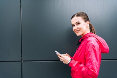 Gülümseyen çekici genç kadın akıllı telefonu sokakta tutuyor.