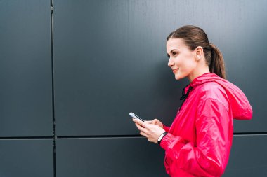 Gülümseyen sporcu kadının sokakta akıllı telefon tutuşu yan görünüm