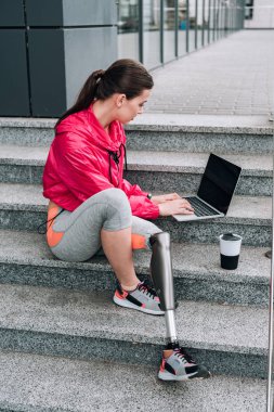 Sokakta merdivenlerde otururken boş ekran kullanan engelli sporcu kadın